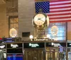 The image depicts the iconic gold-toned clock above the Information Booth in Grand Central Terminal with an American flag hanging in the background