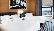 The image shows a modern hotel room with two queen-sized beds, an abstract black and white painting above the headboard, a large window, and a patterned carpet.
