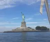 This is a daytime photo featuring the Statue of Liberty viewed from a boat with clear skies and a section of the boats rigging visible in the frame