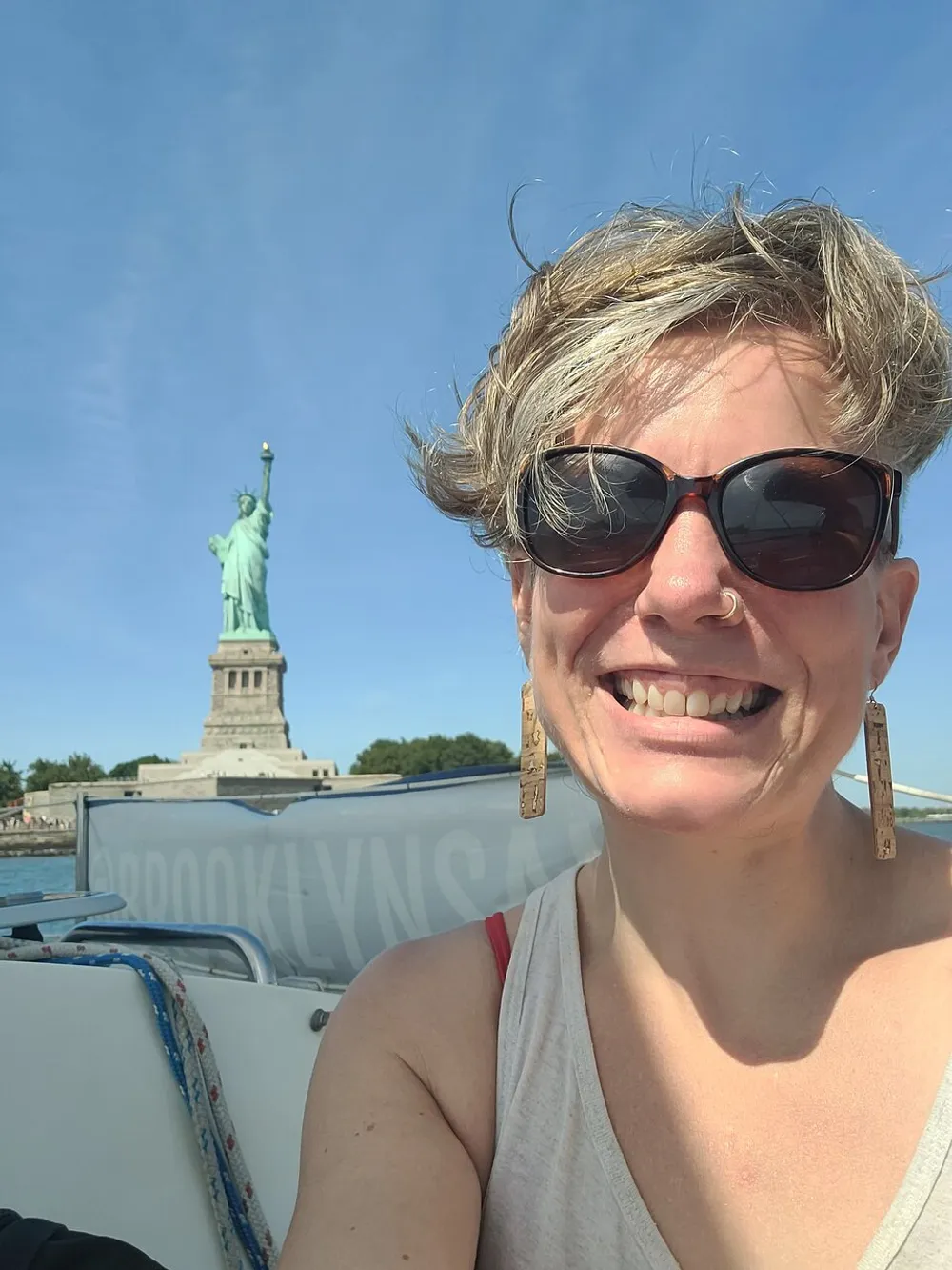 A person is taking a selfie with the Statue of Liberty in the background apparently on a boat