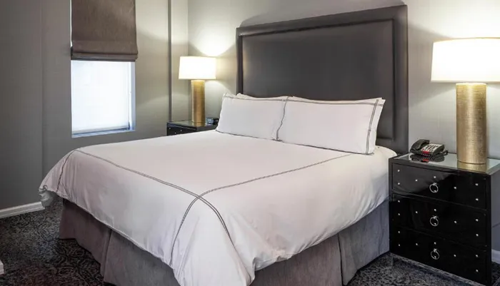The image shows a neatly made bed with white linens in a modern hotel room with two bedside lamps and a phone