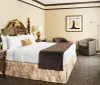 The image shows a well-appointed hotel room with classic-style furniture a plush bed elegant lamps and abstract art on the wall