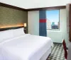 This image shows a modern hotel room with a large bed stylish decor and a window offering a view of an urban skyline