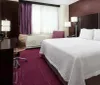 This image shows a tidy and modern hotel room with a large bed a desk with a chair a flat-screen TV and purple accents in the decor