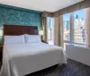 A modernly furnished hotel room with a large bed and a view of a city skyline through the window