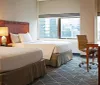 This is an image of a well-appointed double-bed hotel room with a work desk large windows offering a view of high-rise buildings and modern decor