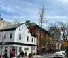 The image shows a charming street lined with historic-looking buildings and patchy spring foliage under a clear blue sky