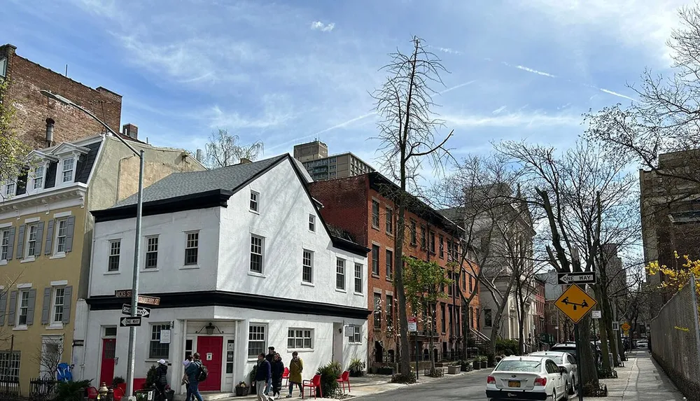 The image shows a charming street lined with historic-looking buildings and patchy spring foliage under a clear blue sky