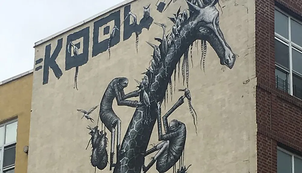 The image showcases a large intricate mural of a giraffe with various insects climbing on its neck painted on the side of a building