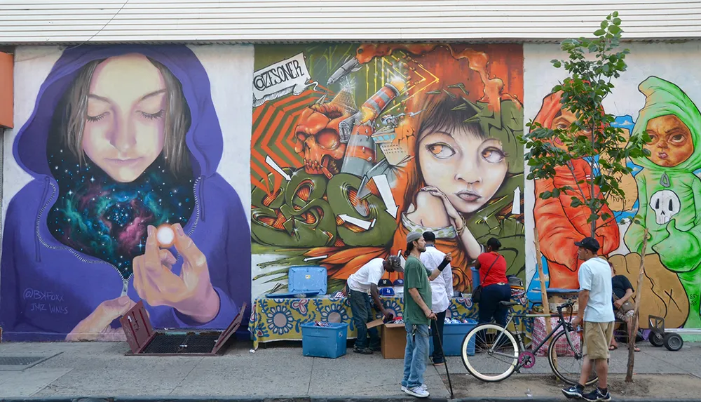 A group of people is seen in front of a vibrant street mural featuring an ethereal figure with a galaxy within her hands juxtaposed with other colorful and fantastical elements