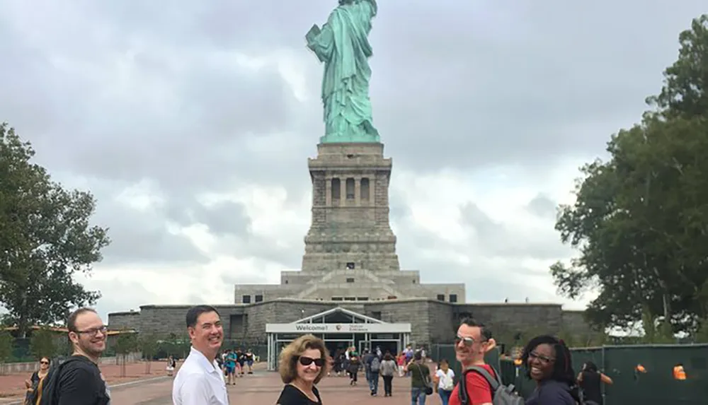 Visitors are posing for a photo in front of the Statue of Liberty on an overcast day