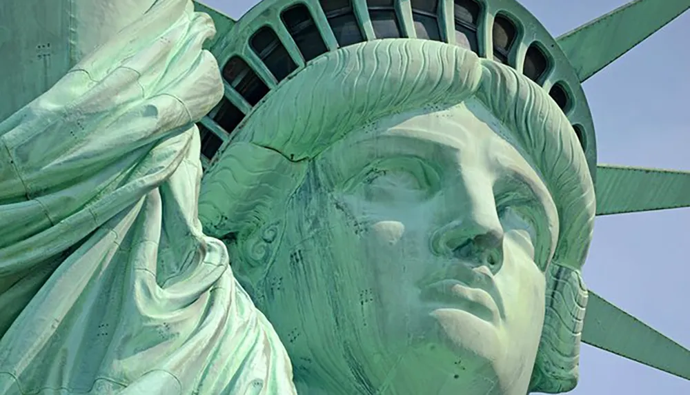 The image shows a close-up of the face of the Statue of Liberty highlighting the detailed sculptural work of the iconic copper monument