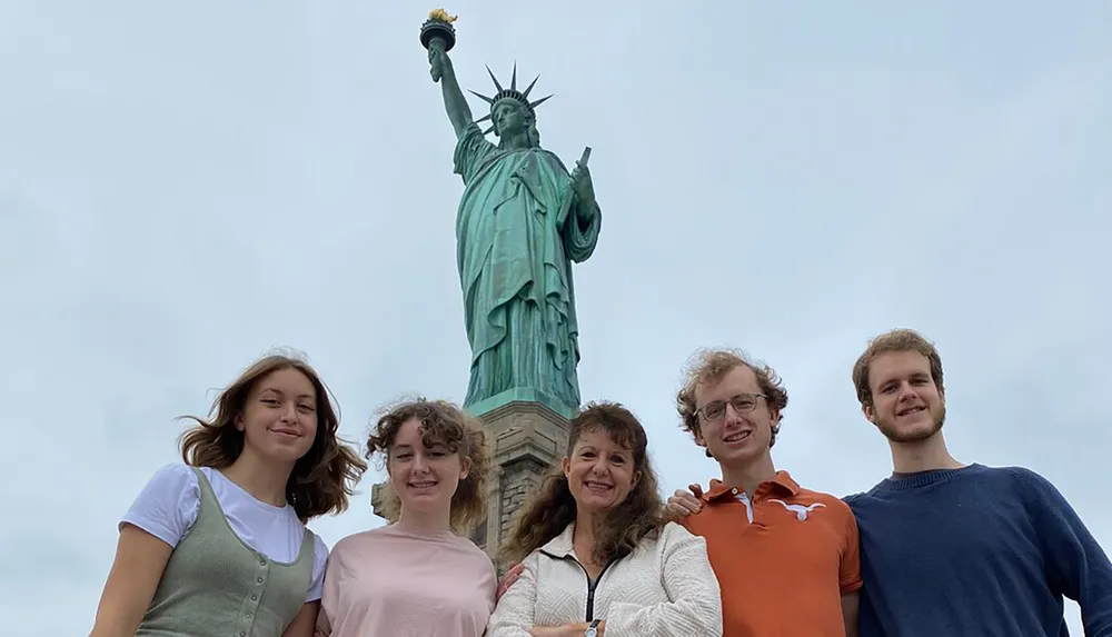 A group of five individuals is posing for a photo with the Statue of Liberty towering in the background