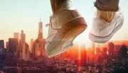 A pair of shoes against a city skyline with the impression of someone jumping or floating above the urban landscape at sunset.
