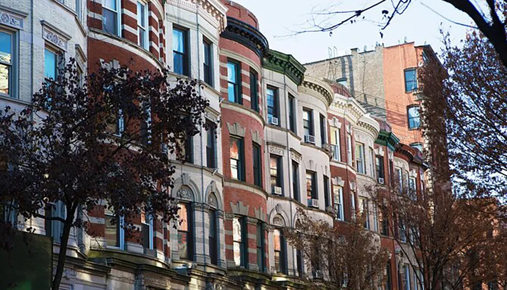 This image shows a row of ornate multistory residential buildings with bay windows and a mix of red brick and stone facades typical of certain historic urban neighborhoods