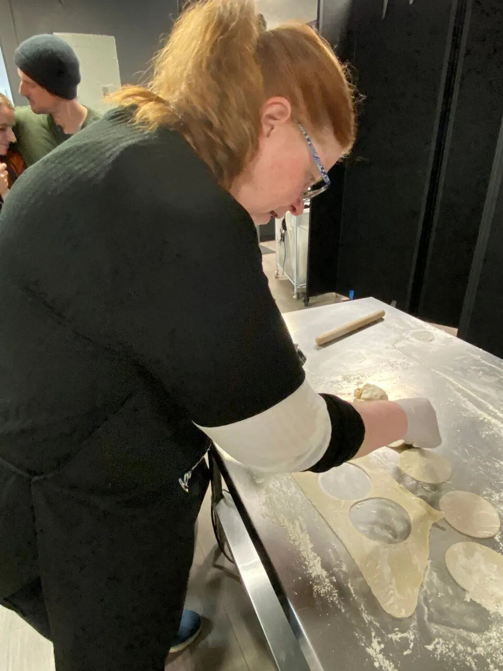 A person is focused on rolling out dough on a floured surface possibly making pastry or pasta