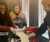 Three people are enjoying a cooking class using a pasta maker to roll out dough with aprons on that read SELFUP