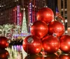 The image showcases a festive display of larger-than-life red Christmas ornaments in front of Radio City Music Hall illuminated by the glow of holiday lights at night