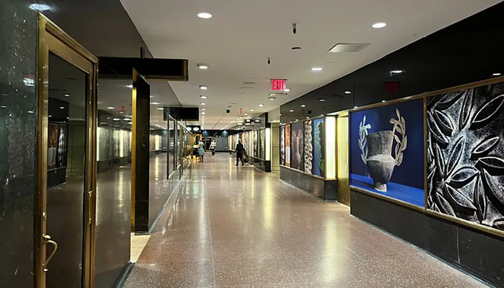 The image shows an indoor corridor with reflective floors framed artwork on the right wall and a few people in the distance creating a quiet and cultured atmosphere