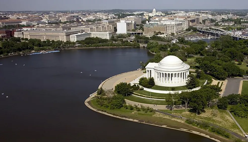 The image shows an aerial view of the Jefferson Memorial located by the Tidal Basin in Washington DC with the cityscape and Capitol building in the background