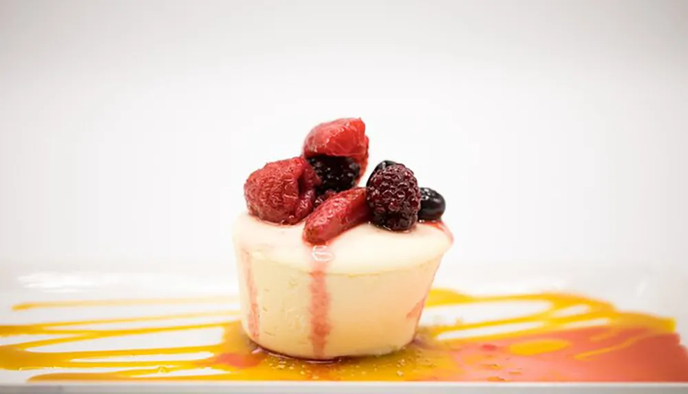 This is an image of a creamy dessert possibly a panna cotta topped with ripe berries and garnished with a vibrant colorful sauce