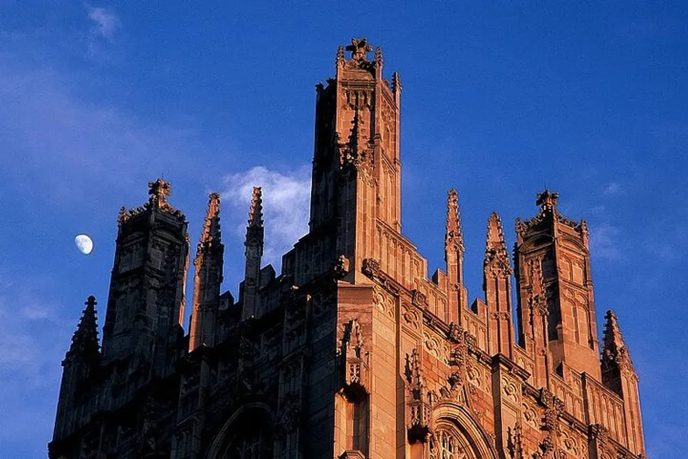 The image shows a gothic-style building with intricate spires against an evening sky accompanied by the waxing crescent moon