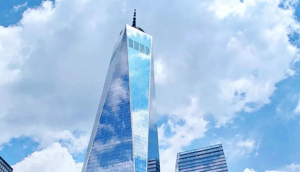 The image shows a tall skyscraper with a reflective glass facade reaching into a cloudy blue sky surrounded by other buildings