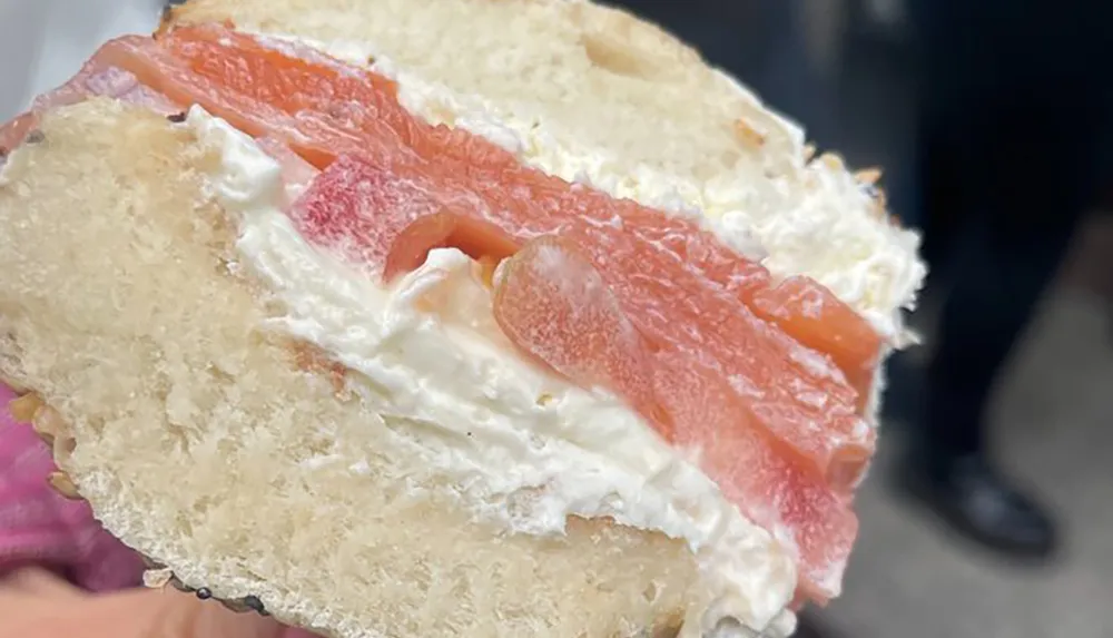 The image shows a close-up view of a halved bagel sandwich with a generous amount of cream cheese and slices of smoked salmon