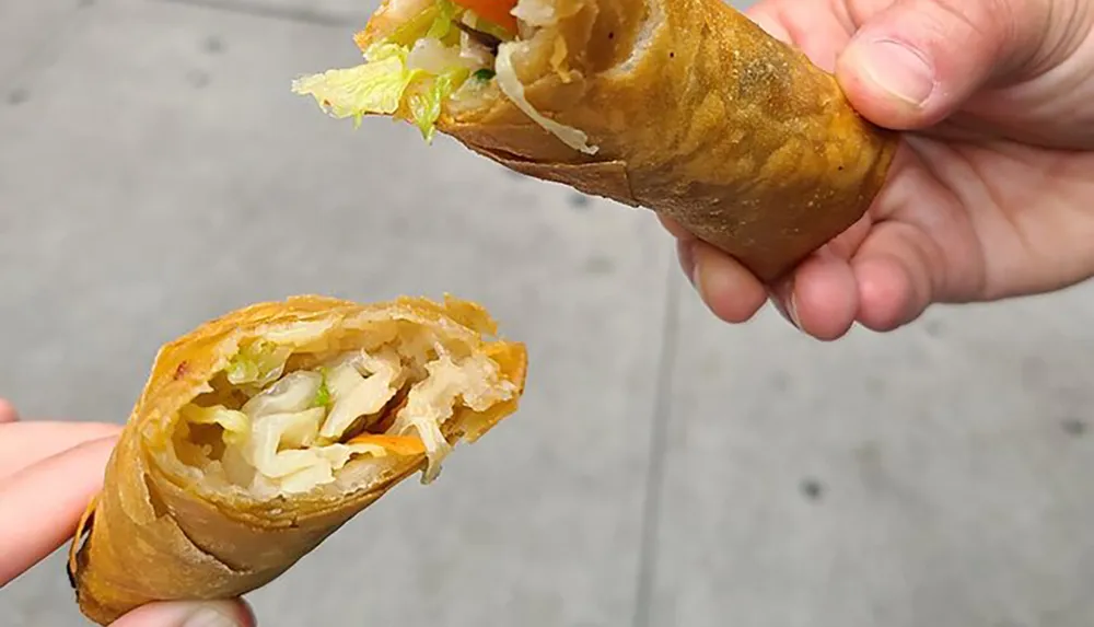 A person is holding a half-eaten egg roll revealing its vegetable filling