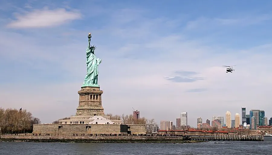 The image shows the Statue of Liberty with a helicopter flying by and a city skyline in the background.