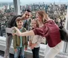 A family is taking a selfie with a smartphone against the backdrop of a panoramic city view from a high vantage point