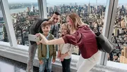 A family is taking a selfie with a smartphone against the backdrop of a panoramic city view from a high vantage point.