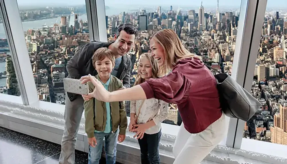 A family is taking a selfie with a smartphone against the backdrop of a panoramic city view from a high vantage point