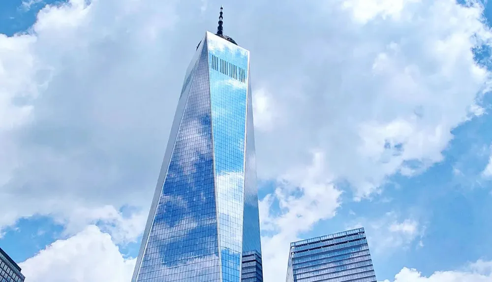 The image shows a large reflective skyscraper towering into a cloudy blue sky