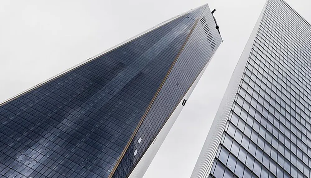 The image shows a low-angle view of two high-rise buildings with glass facades against a cloudy sky