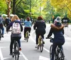 A group of smiling people are positioned on bicycles on an urban street wearing casual attire and conference lanyards