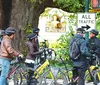 A group of smiling people are positioned on bicycles on an urban street wearing casual attire and conference lanyards