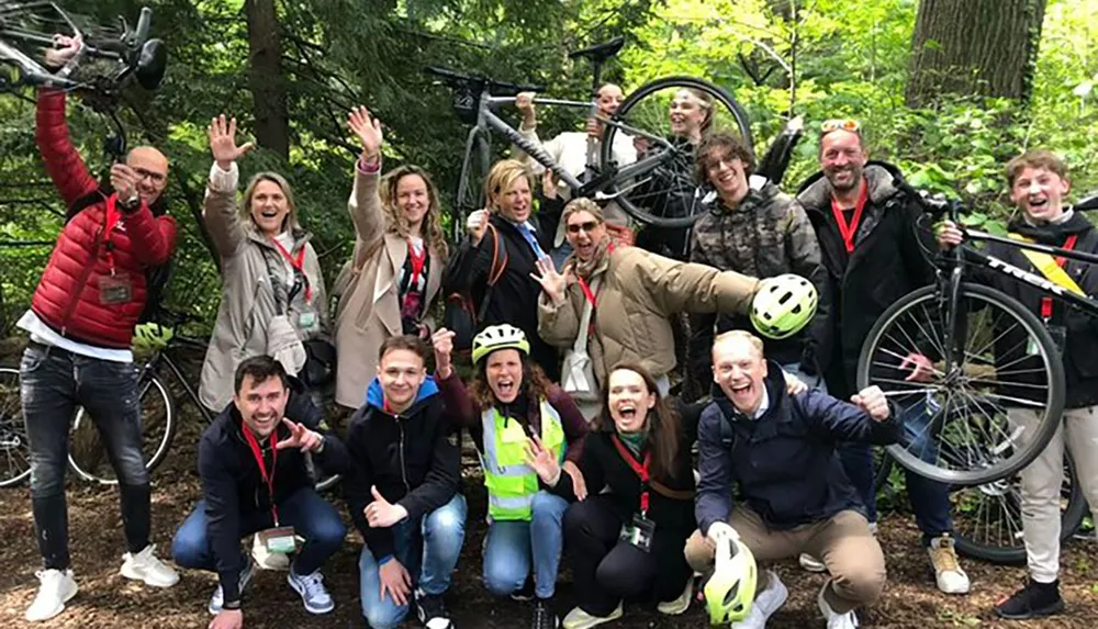 A group of jubilant people are posing with bicycles in a forest smiling and making playful gestures for the camera