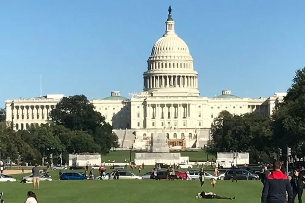 The image shows people enjoying a sunny day on the grass with the United States Capitol building in the background