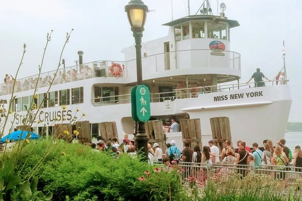 A large group of people is boarding the Miss New York cruise ship while others enjoy the upper deck with a pedestrian sign in the foreground indicating a shared walkway for people and cyclists
