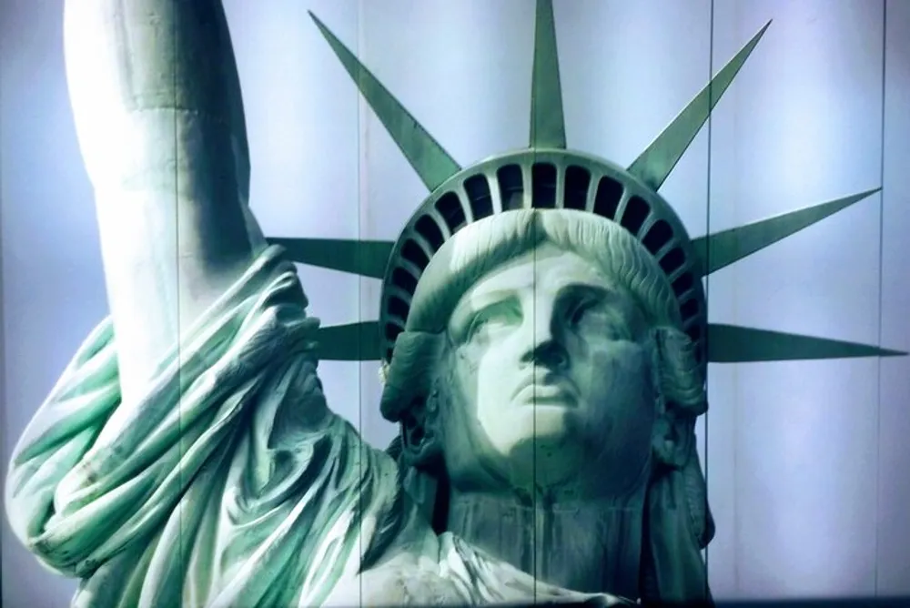 The photo shows a close-up view of the Statue of Liberty focusing on the head and crown with a raised torch visible to the left