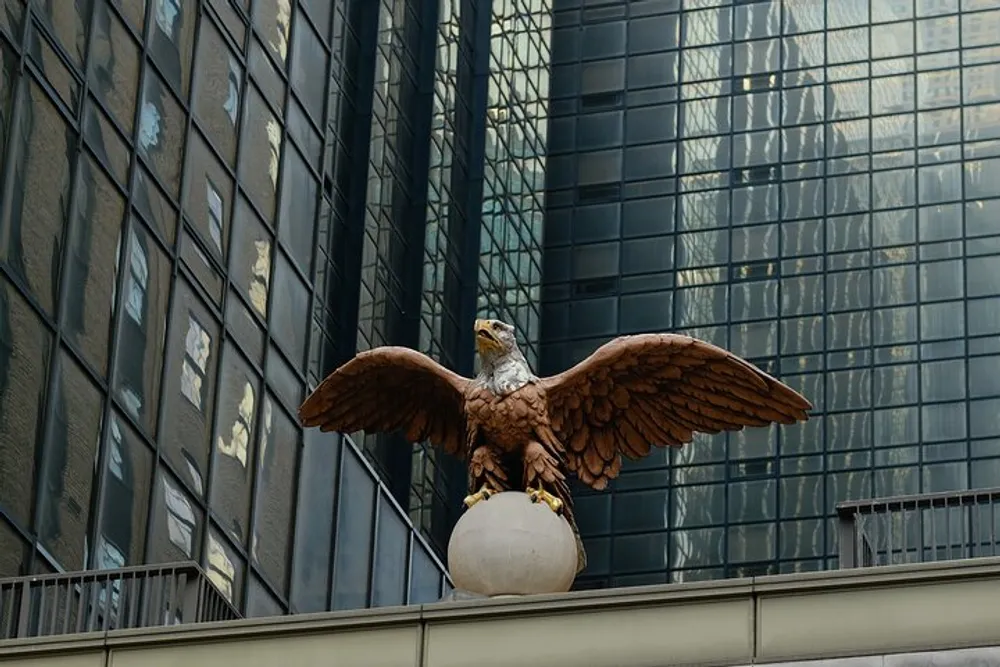 An eagle statue with outstretched wings perched atop a pedestal against the backdrop of a modern glass skyscraper