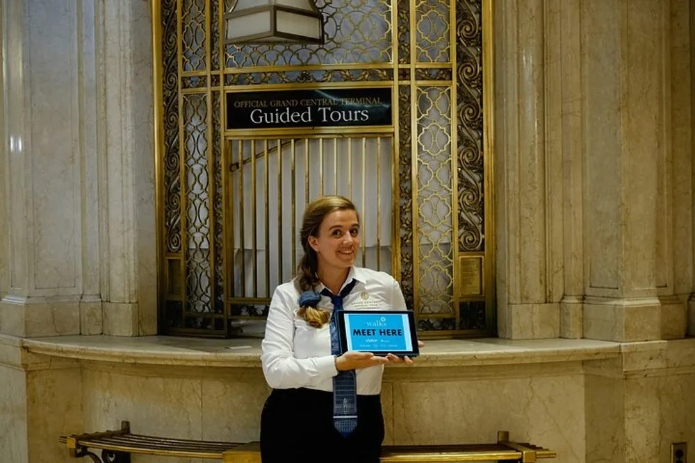 A person is standing in a grand interior holding a Meet Here sign for Official Grand Central Terminal Guided Tours