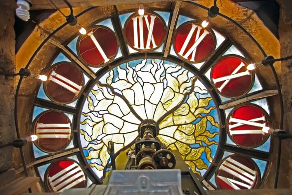 The image features a magnificent stained glass window with a radiating design framed by circular patterns of red and white and accentuated by hanging light bulbs