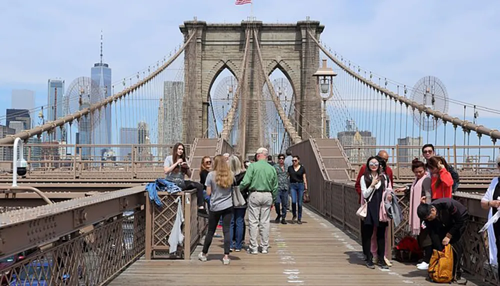 Pedestrians are walking across the Brooklyn Bridge with the Manhattan skyline in the background on a clear day
