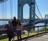 Three people are posing for a photo in front of a striking suspension bridge on a sunny day