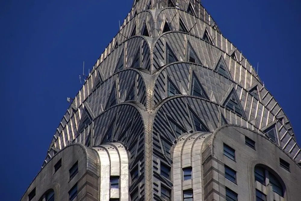 The image shows a close-up of the distinctive terraced crown of the Chrysler Building an iconic art deco skyscraper set against a clear blue sky