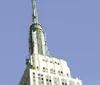 The image shows the top portion of the Empire State Building against a clear blue sky