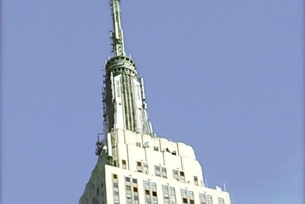 The image shows the top portion of the Empire State Building against a clear blue sky