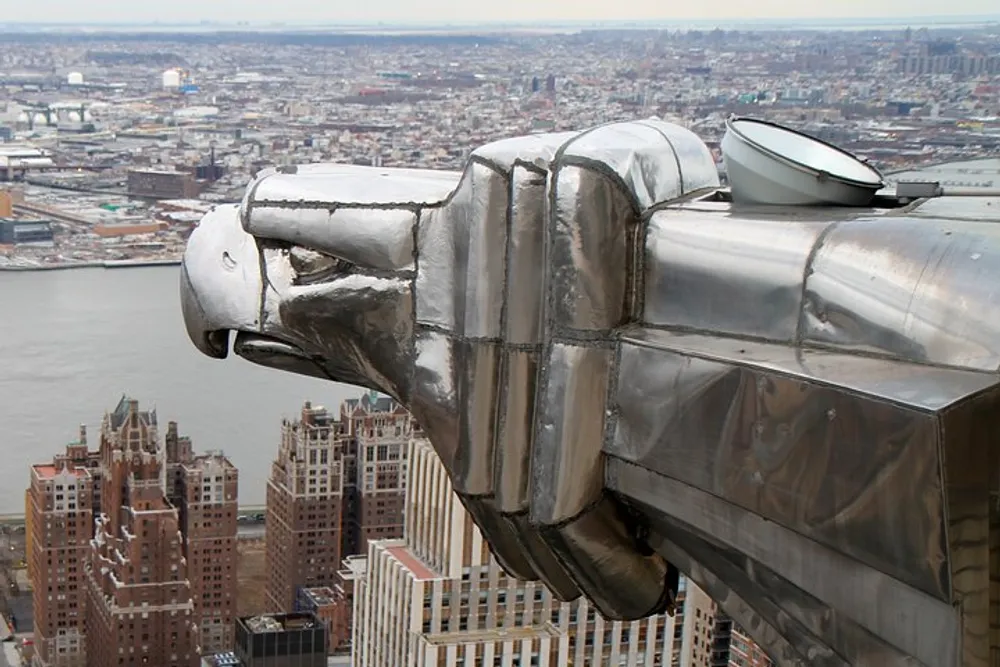 The image reveals a close-up view of a metal eagle gargoyle ornamentation jutting out from a high vantage point with a sweeping view of a densely built urban landscape in the background